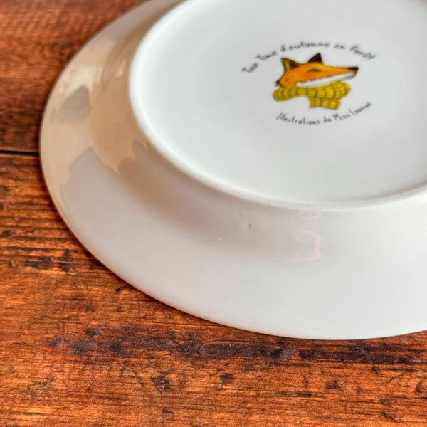 Assiette en porcelaine avec illustration décalée sur le côté et défaut en dessous « Tea time d'automne en forêt »